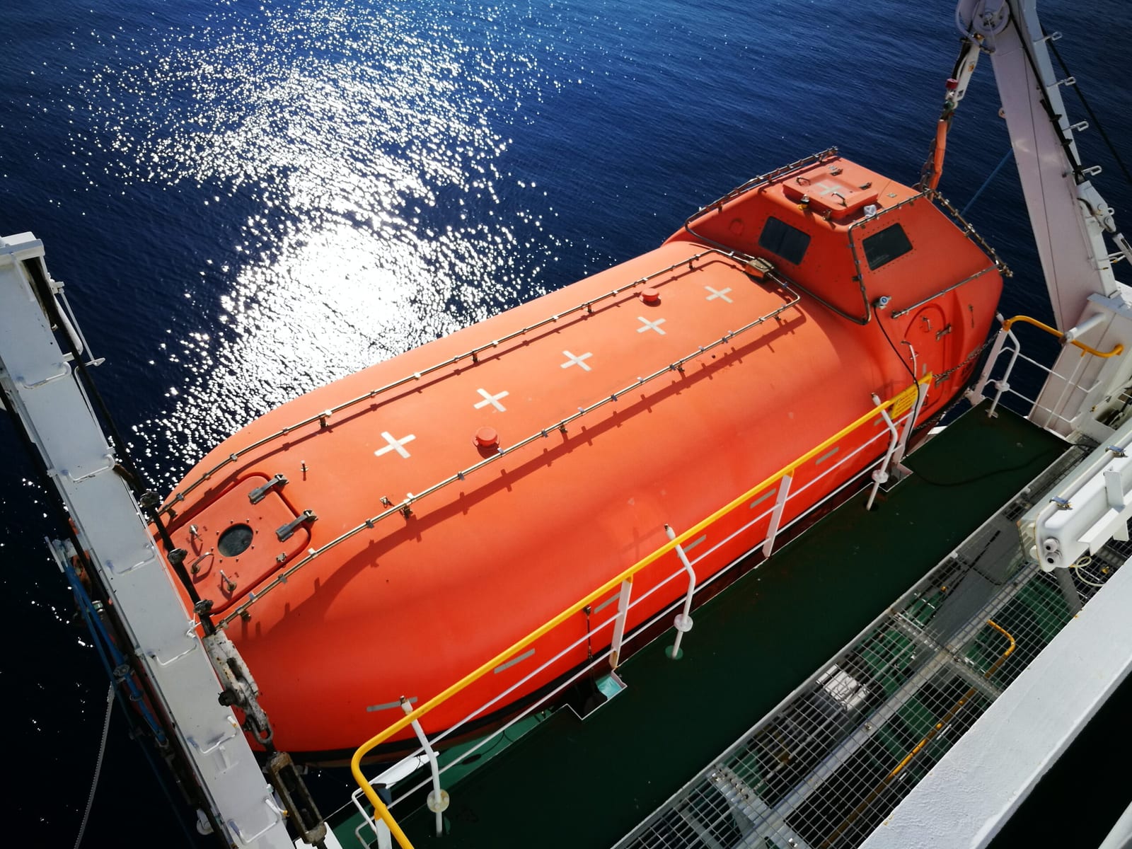 Enclosed lifeboat being lowered on its davits during deployment testing